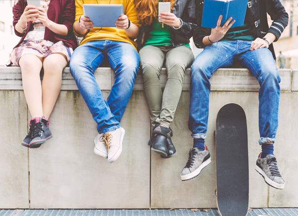 Eine Gruppe Jugendlicher sitzt auf einer Mauer und verwendet Geräte.