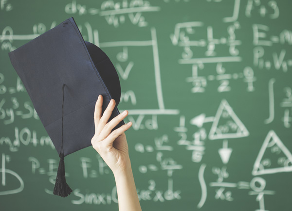 Eine Hand hebt eine Abschlusskappe vor einer Tafel mit Formeln.